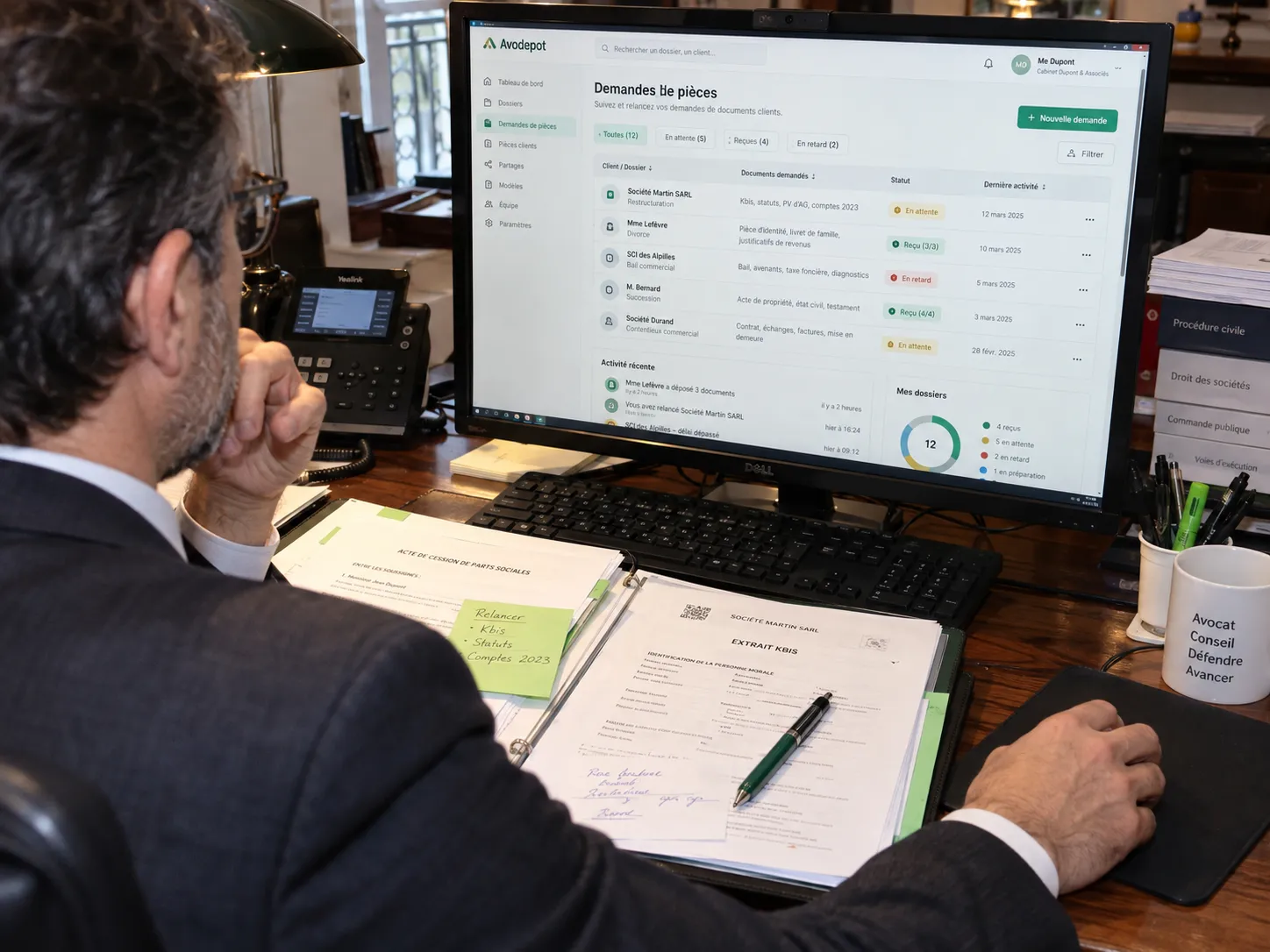 Un avocat consulte un dossier de pièces sur son écran, un classeur ouvert devant lui.